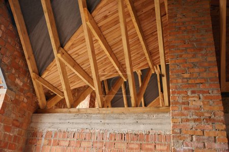 Photo for Interior view of unfinished garret room with wooden roof trusses and red brick walls - Royalty Free Image