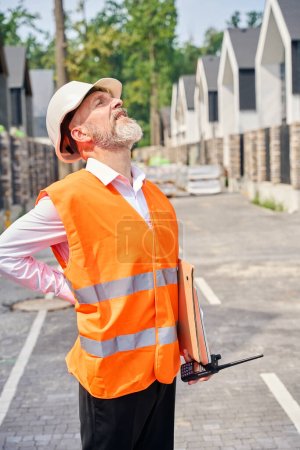 Photo for Construction supervisor with walkie-talkie in hand standing in middle of street between rows of residential houses - Royalty Free Image