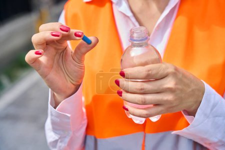 Photo for Cropped photo of construction supervisor holding drug capsule and plastic bottle of water in hands while standing outdoors - Royalty Free Image