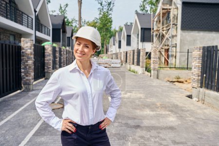 Photo for Smiling building site manager standing in middle of paved street between rows of unfinished private residential houses - Royalty Free Image