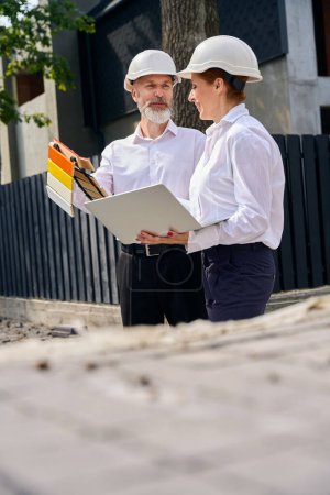 Photo for Customer with facade paint sample boards in hands talking to architectural designer on construction site - Royalty Free Image