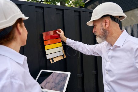 Téléchargez les photos : Panneaux d'échantillons de peinture inclinables du client contre une clôture en bois en présence de concepteur architectural sur le chantier - en image libre de droit