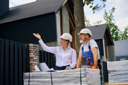 Photo for Building inspector pointing at house exterior to builder during construction site inspection - Royalty Free Image