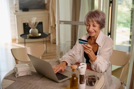 Téléchargez les photos : Mignon femme plus âgée fait des achats en ligne, elle utilise un ordinateur portable - en image libre de droit