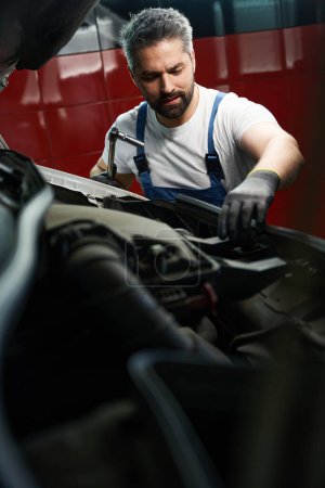 Photo for Serious concentrated auto mechanic inspecting motor vehicle parts under bonnet - Royalty Free Image