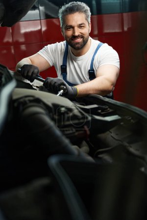 Photo for Smiling automotive service technician is tightening parts on customer motor vehicle using wrench - Royalty Free Image