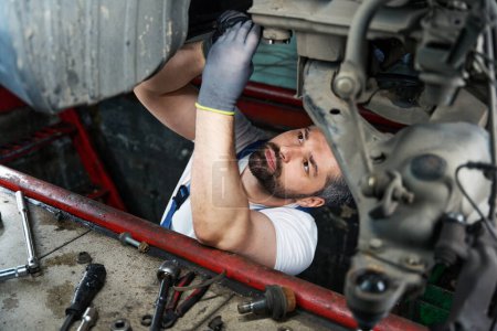 Photo for Concentrated car mechanic is tightening nut on motor vehicle underbody using spanner - Royalty Free Image