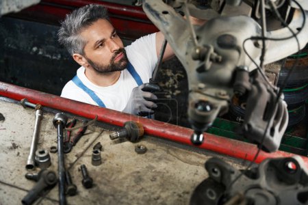 Photo for Serious automobile repair shop worker tightening parts on vehicle underside with spanner - Royalty Free Image