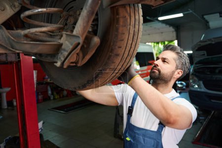 Foto de Mecánico experto que lleva a cabo la inspección de neumáticos en el coche del cliente en taller de reparación de automóviles - Imagen libre de derechos