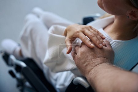 Téléchargez les photos : Homme médecin main touchant épaule d'une patiente handicapée assise en fauteuil roulant - en image libre de droit
