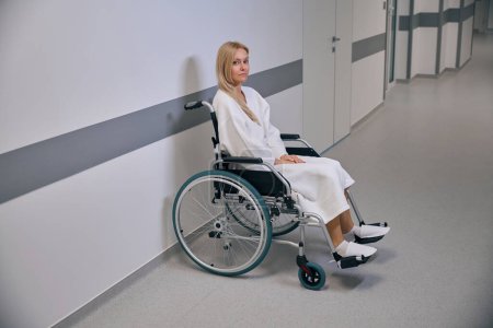 Téléchargez les photos : Femme faible d'esprit handicapée assise dans un fauteuil roulant près d'un mur dans un couloir d'un établissement pour malades hospitalisés - en image libre de droit