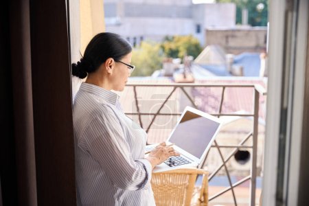 Foto de Mujer con lápiz en la mano escribiendo en un ordenador portátil mientras está sola en el balcón - Imagen libre de derechos