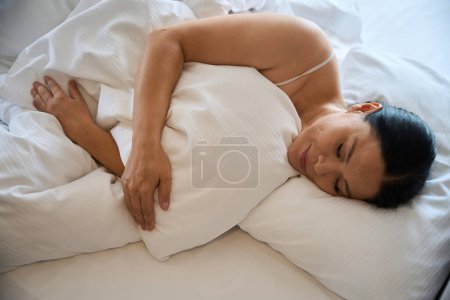 Téléchargez les photos : Tranquille femme couchée dans un lit confortable avec les yeux fermés enveloppé dans une couverture - en image libre de droit