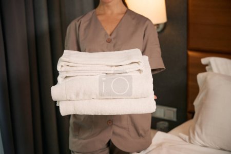 Photo for Cropped photo of maid in uniform holding stack of clean towels in her hands - Royalty Free Image