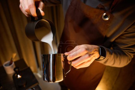 Foto de Cafetera irreconocible o camarero vertiendo leche de jarra preparando café en la cafetería - Imagen libre de derechos