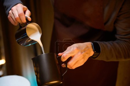 Foto de Manos de barista vertiendo leche de jarra preparando delicioso café en la cafetería - Imagen libre de derechos