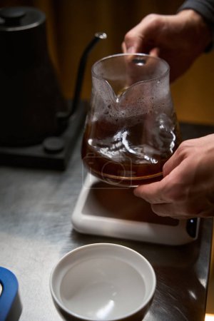 Téléchargez les photos : Barista mâle anonyme versant Americano aromatique chaud de cuisinière cafetière dans la tasse placée sur le comptoir dans le café - en image libre de droit