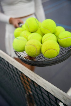 Foto de Mujer irreconocible sosteniendo muchas pelotas de tenis en raqueta de pie en la cancha - Imagen libre de derechos