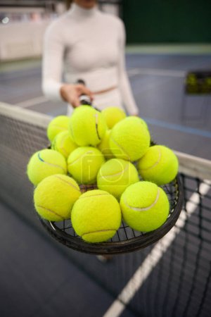 Téléchargez les photos : Joueuse inconnue en tenue blanche tenant beaucoup de balles de tennis sur la raquette se préparant pour l'entraînement - en image libre de droit