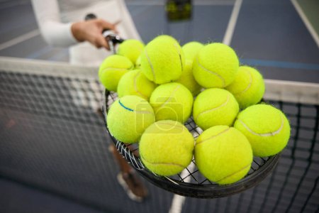 Téléchargez les photos : Joueuse méconnaissable tenant beaucoup de balles de tennis sur la raquette se préparant pour l'entraînement - en image libre de droit