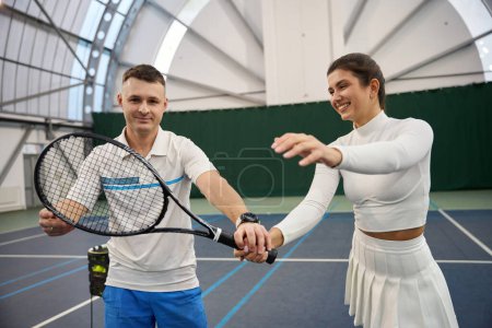Foto de Joven hombre enseñando a la mujer cómo agarrar raqueta de tenis jugando en la cancha cubierta - Imagen libre de derechos