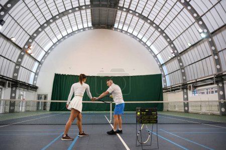 Foto de Mujer deportiva y hombre instructor jugando tenis se centra en golpear mejorar las habilidades en la cancha cubierta - Imagen libre de derechos
