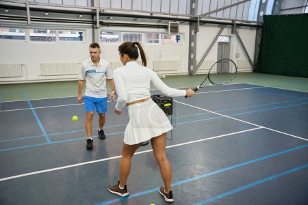 Téléchargez les photos : Homme sportif instructeur avec une femme jouant au tennis améliorer les compétences apprendre à frapper sur le terrain intérieur - en image libre de droit