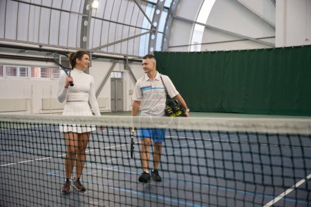 Téléchargez les photos : Fit femme avec l'homme instructeur après avoir joué au tennis jeu à court intérieur - en image libre de droit
