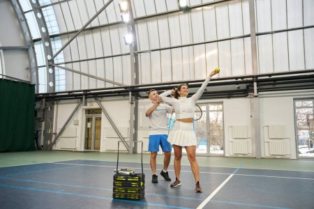 Téléchargez les photos : Homme instructeur se concentrant sur l'enseignement de la technique de service à la joueuse de tennis - en image libre de droit
