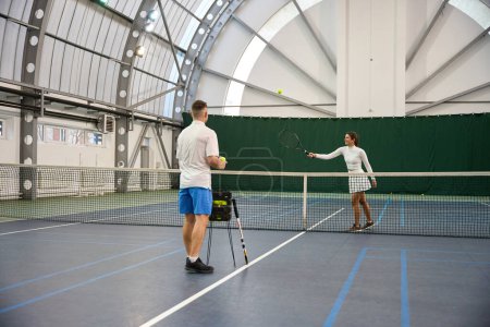 Photo for Man trainer engages with woman learner working for improving serving skills on indoor court - Royalty Free Image