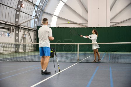 Photo for Man coach instructs beginner in serving emphasizing importance of concentration on indoor court - Royalty Free Image