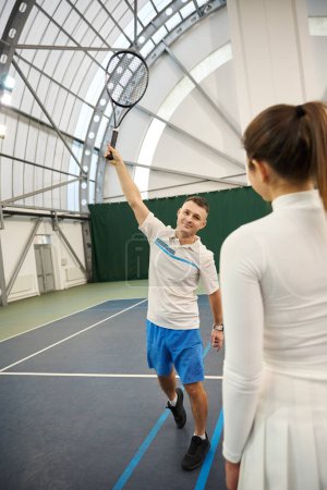 Foto de Hombre instructor y mujer aprendiz en la sesión de tenis mejorar las habilidades de servicio en la cancha cubierta - Imagen libre de derechos