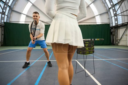 Photo for Man coach explaining serving balls to woman player beginner on indoor court - Royalty Free Image
