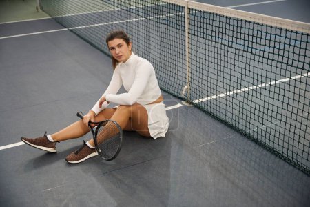 Photo for Sporty woman with racket in hands sitting on tennis court - Royalty Free Image