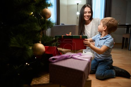 Photo for Beautiful smiling woman celebrating Christmas with her son sharing presents New Year tree in hotel - Royalty Free Image