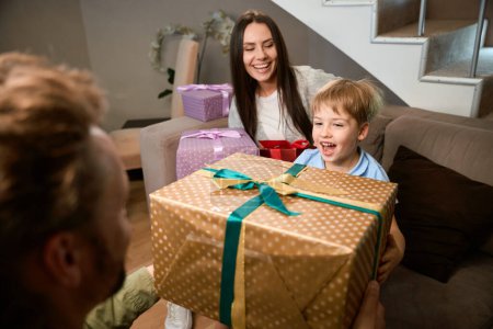 Foto de Hombre dando regalo a su pequeño hijo mientras celebra las vacaciones de Navidad con la familia en casa - Imagen libre de derechos