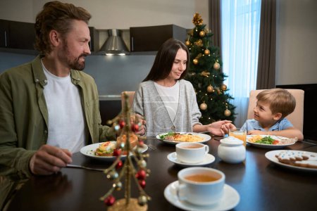 Photo for Joyful family holding hands and praying before festive Christmas dinner at home - Royalty Free Image