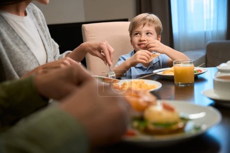 Photo for Cute cheerful boy having festive dinner in hotel with his mother and father celebrating Christmas together - Royalty Free Image