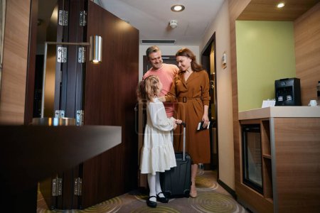 Photo for Caucasian family of mother, father and daughter with suitcase entering hotel room. Concept of rest, vacation and travelling. Idea of family relationship and spending time together - Royalty Free Image