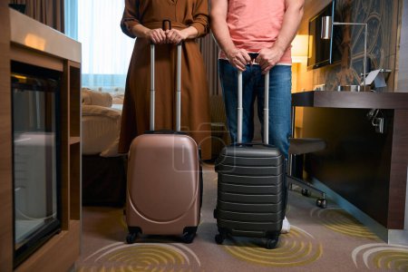 Téléchargez les photos : Vue partielle de face du couple avec valises dans la chambre d'hôtel. Concept de repos, vacances et voyages - en image libre de droit