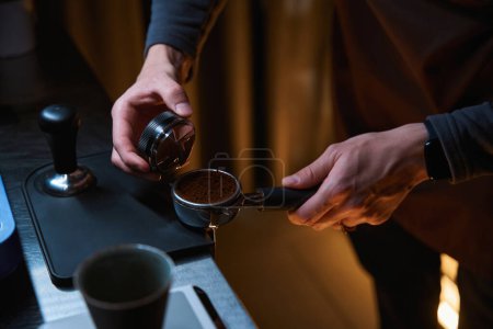 Photo for Unrecognizable coffee maker hands holding portafilter and coffee tamper making aroma beverage in coffee house - Royalty Free Image