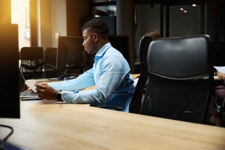 Photo for Back view African American man in elegant blue shirt working on laptop in office with many workplaces, business man involved in applying and office goods ordering, supply department - Royalty Free Image
