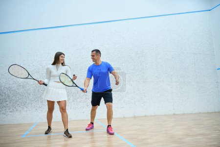 Téléchargez les photos : Femme énergique pratique squash avec l'homme entraîneur améliorer les compétences de jeu sur le terrain intérieur - en image libre de droit