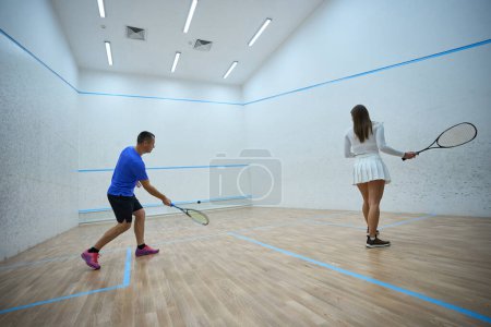 Foto de Energetic sportswoman practica refinar habilidades de golpear con squash man coach en pista cubierta - Imagen libre de derechos