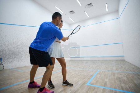 Téléchargez les photos : Femme raffine frapper précision dans la leçon de squash avec l'homme instructeur sur le terrain intérieur - en image libre de droit