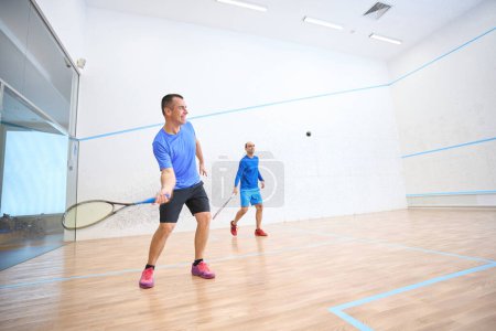 Photo for Sporty men having fun playing squash mixing recreation with fitness on indoor court - Royalty Free Image