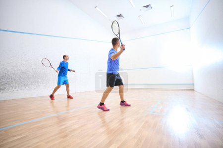 Téléchargez les photos : Hommes sportifs se joignant à la compétition de squash mettant en valeur les compétences sur le terrain intérieur - en image libre de droit