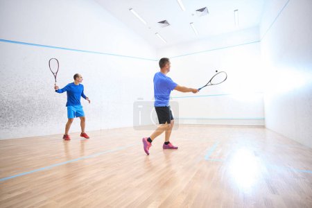 Téléchargez les photos : Des hommes sportifs actifs s'entraînent ensemble sur un terrain de squash intérieur - en image libre de droit