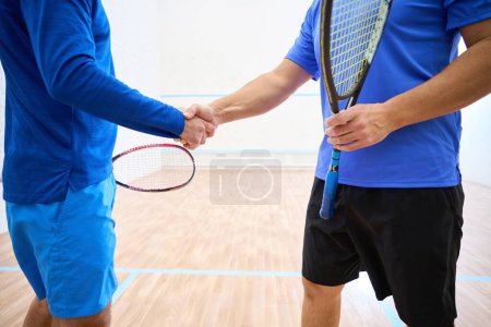 Photo for Two unrecognizable squash players with rackets shaking hands on indoor court - Royalty Free Image