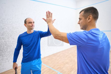 Photo for Two active squash players giving high five after game on indoor court - Royalty Free Image